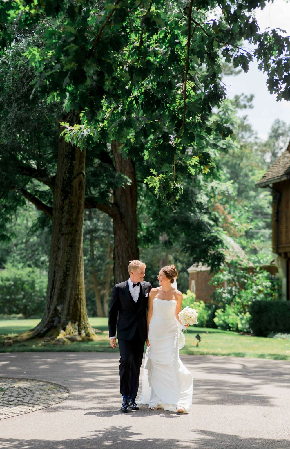 A couple walking along a tree-lined path on their wedding day in an elegant garden setting.