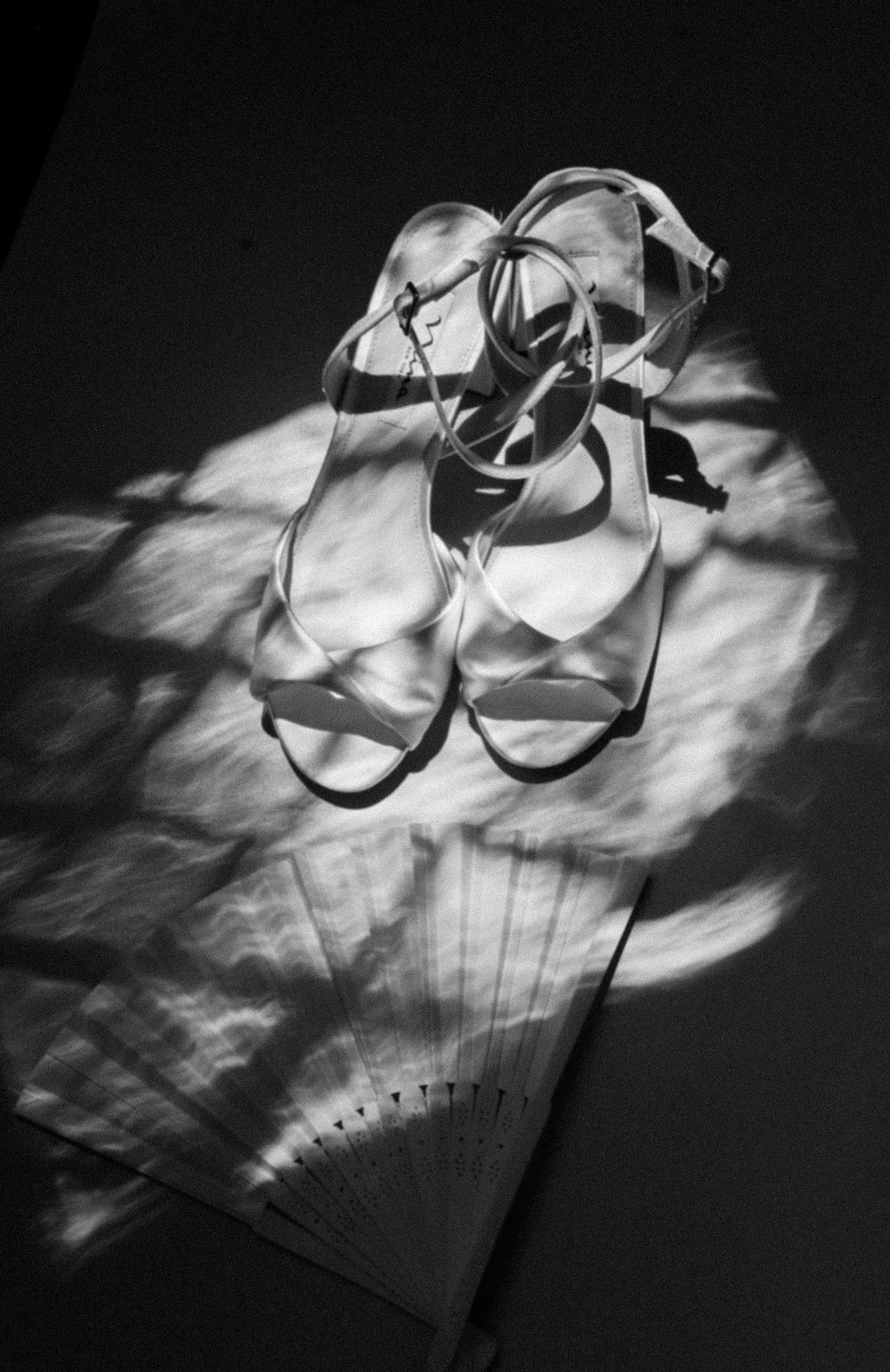 Elegant silver stiletto sandals rest on a decorative folding fan in dramatic black and white lighting.