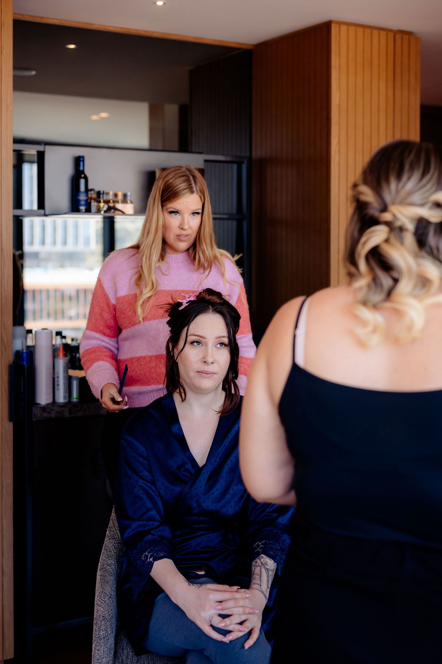 A stylist works on arranging hair in a modern salon with dark and wood-paneled walls and black interior accents.