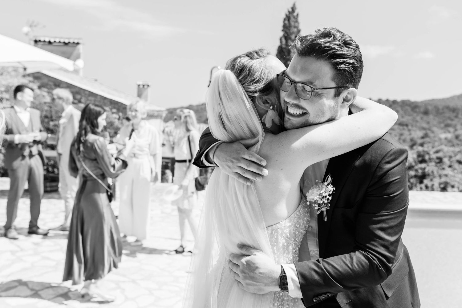 Eine Umarmung zur Gratulation der Braut von einem Gast auf der mallorquinischen Finca Xiclati, festgehalten in Schwarz-Weiß-Fotografie.