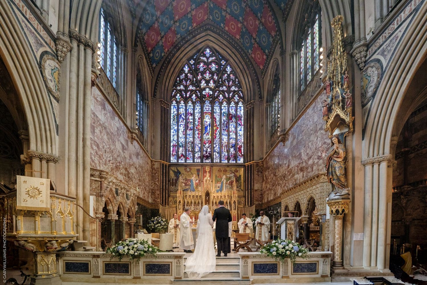 A wedding ceremony taking place in a grand cathedral with ornate stained glass windows and Gothic architecture.