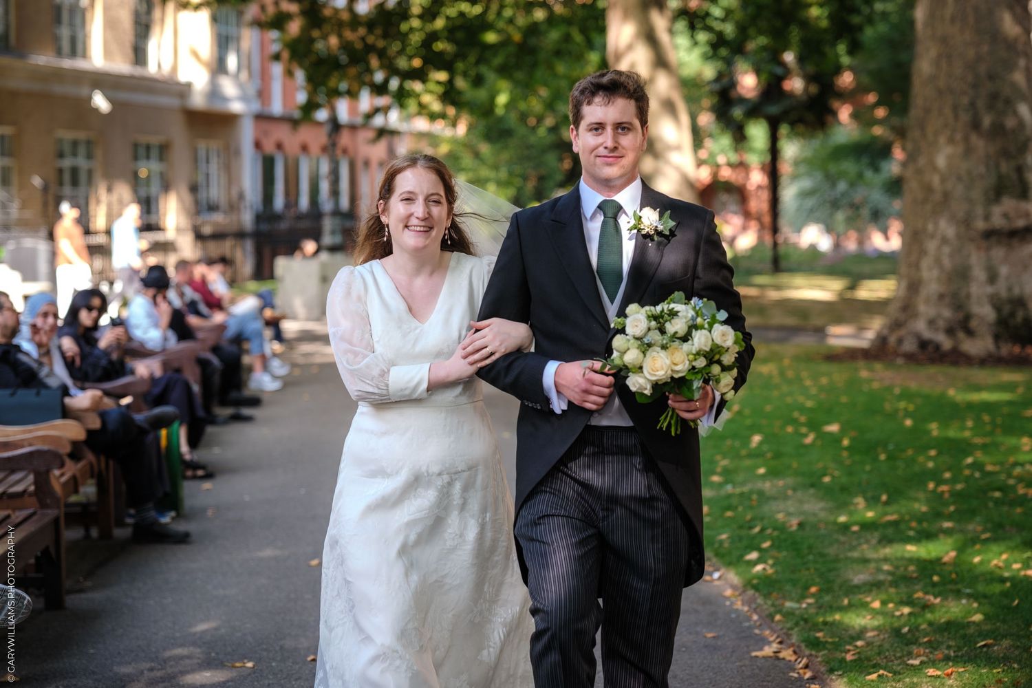 Joyful wedding couple walks arm in arm through a lush garden path during their outdoor celebration.