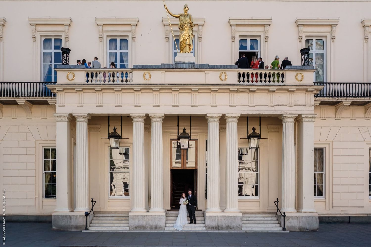 A grand baroque palace exterior with ornate architectural details, golden statues, and rows of elegant windows.