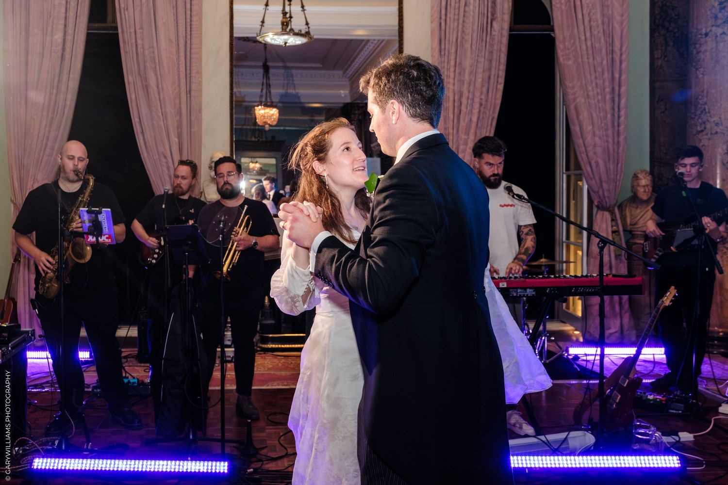 People dancing and celebrating at a lively wedding reception with pink curtains and ambient lighting.