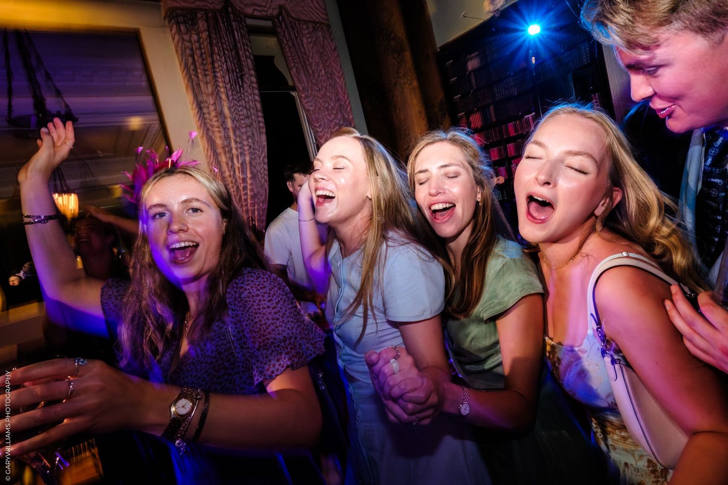 Wedding party guests dancing and laughing under blue party lights on a dark dance floor.