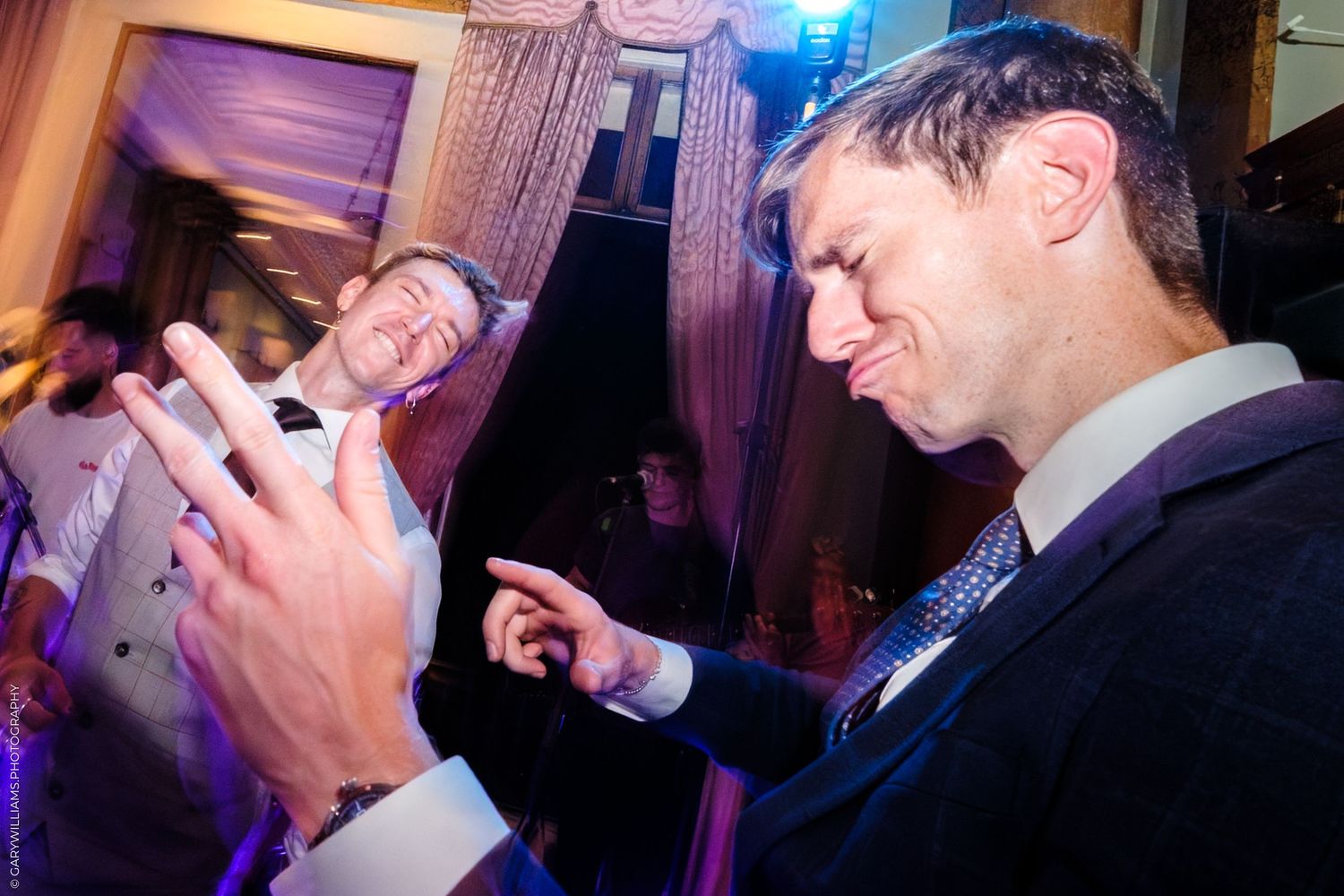People enjoying themselves with drinks and laughter at a dimly lit evening party with blue lighting.