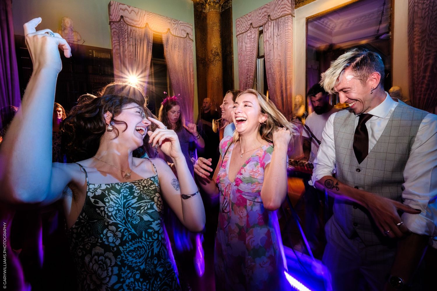 Party guests on a dance floor at a reception with purple lighting creating a lively atmosphere.