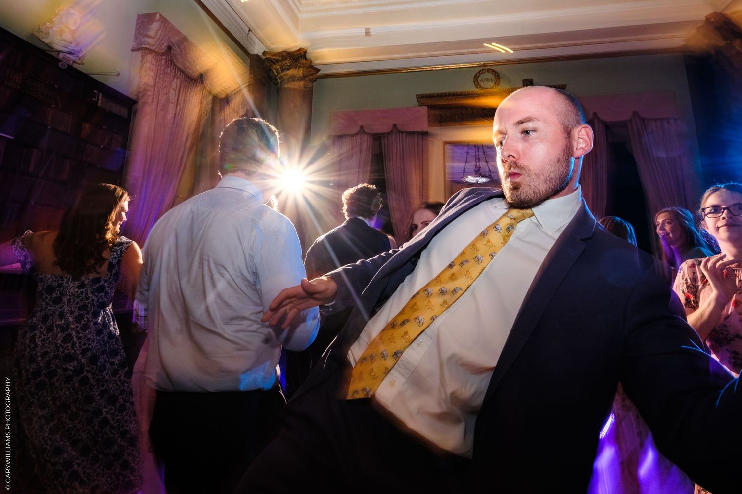 Blurred wedding reception dance floor captures energetic movement of guests celebrating in colorful lighting.