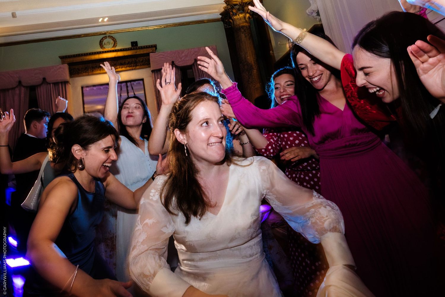 People dancing enthusiastically at a wedding reception with colorful lights and festive atmosphere.