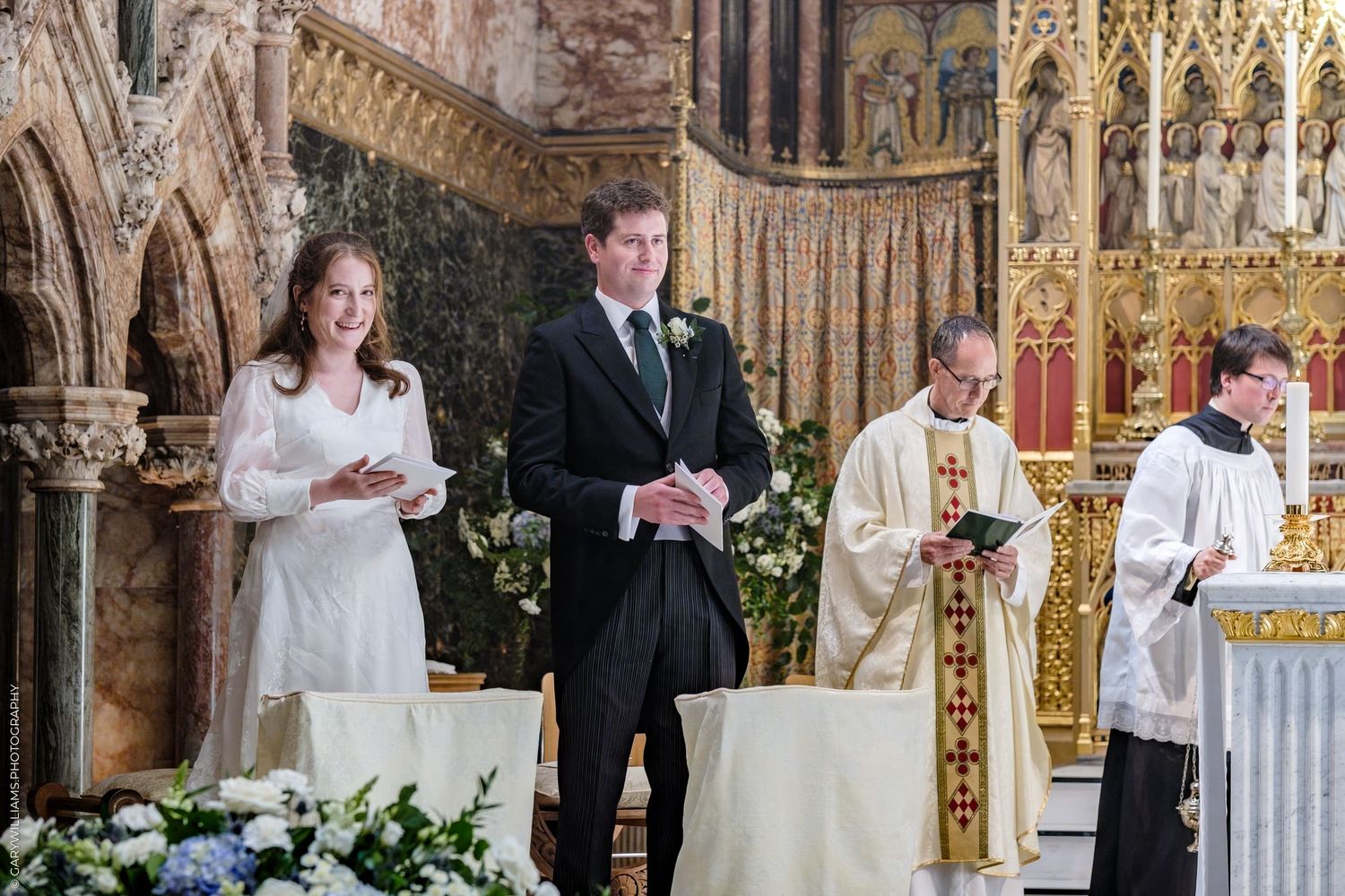 Traditional church wedding ceremony taking place inside ornate Gothic cathedral with detailed stonework and altar decorations.