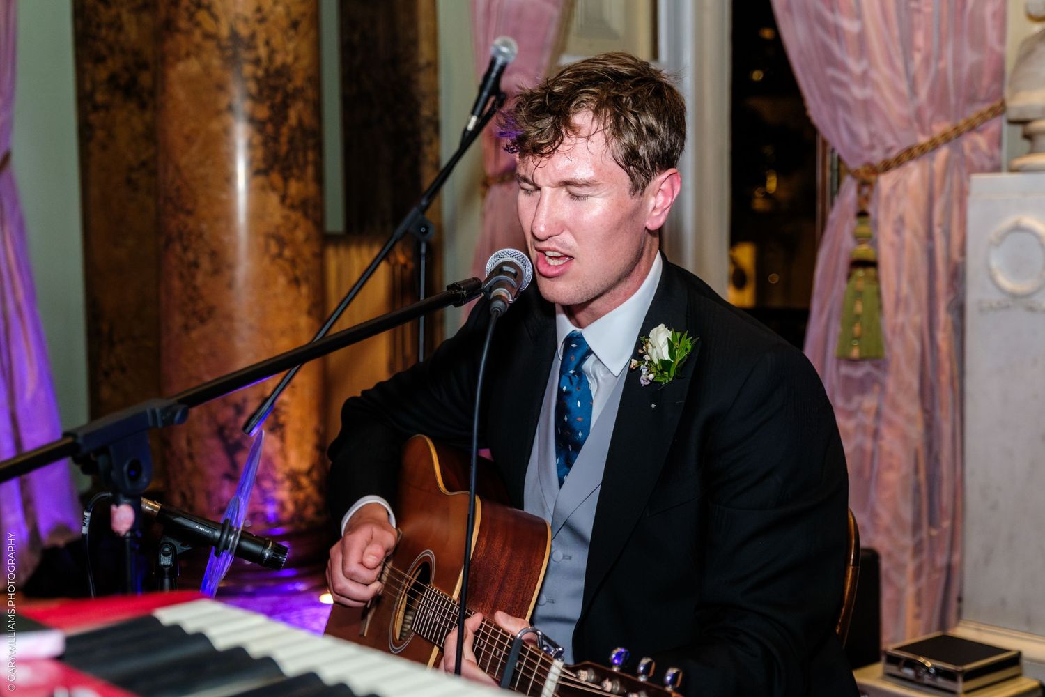 Musicians in formal attire perform live music at an elegant venue with ornate columns.