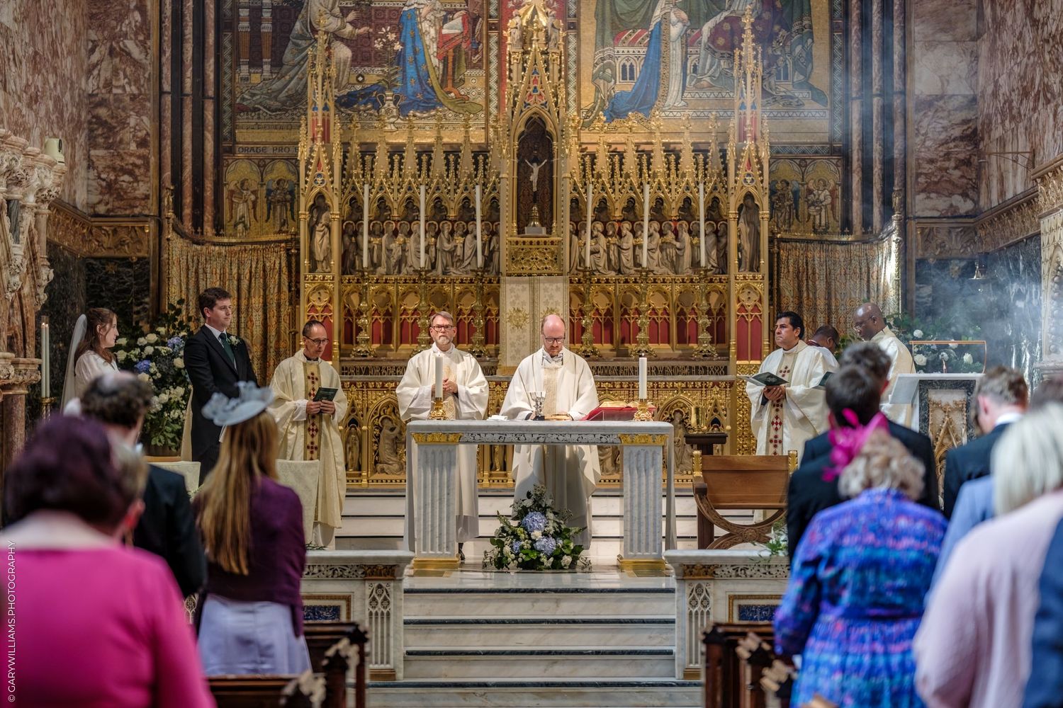 People gather in an ornate Catholic church with gilded altars and decorative architecture during a religious service.