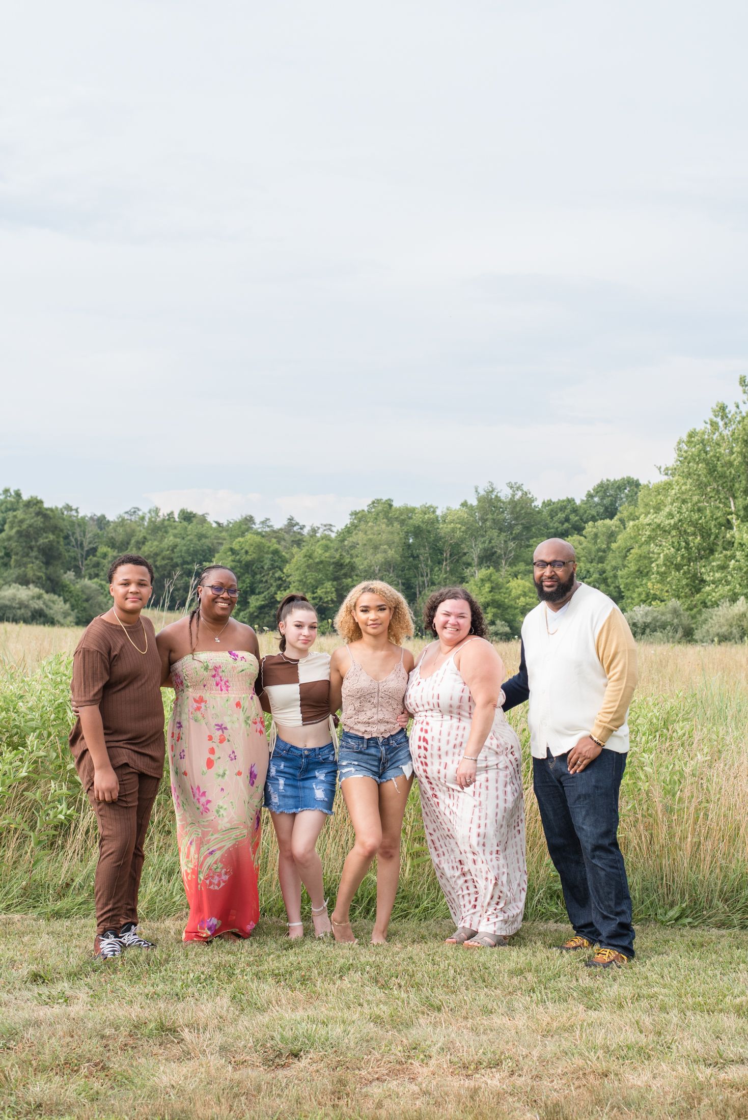 An extended family poses comfortably during a family photo session in a field in northern Virginia, with tall grass and trees in background.