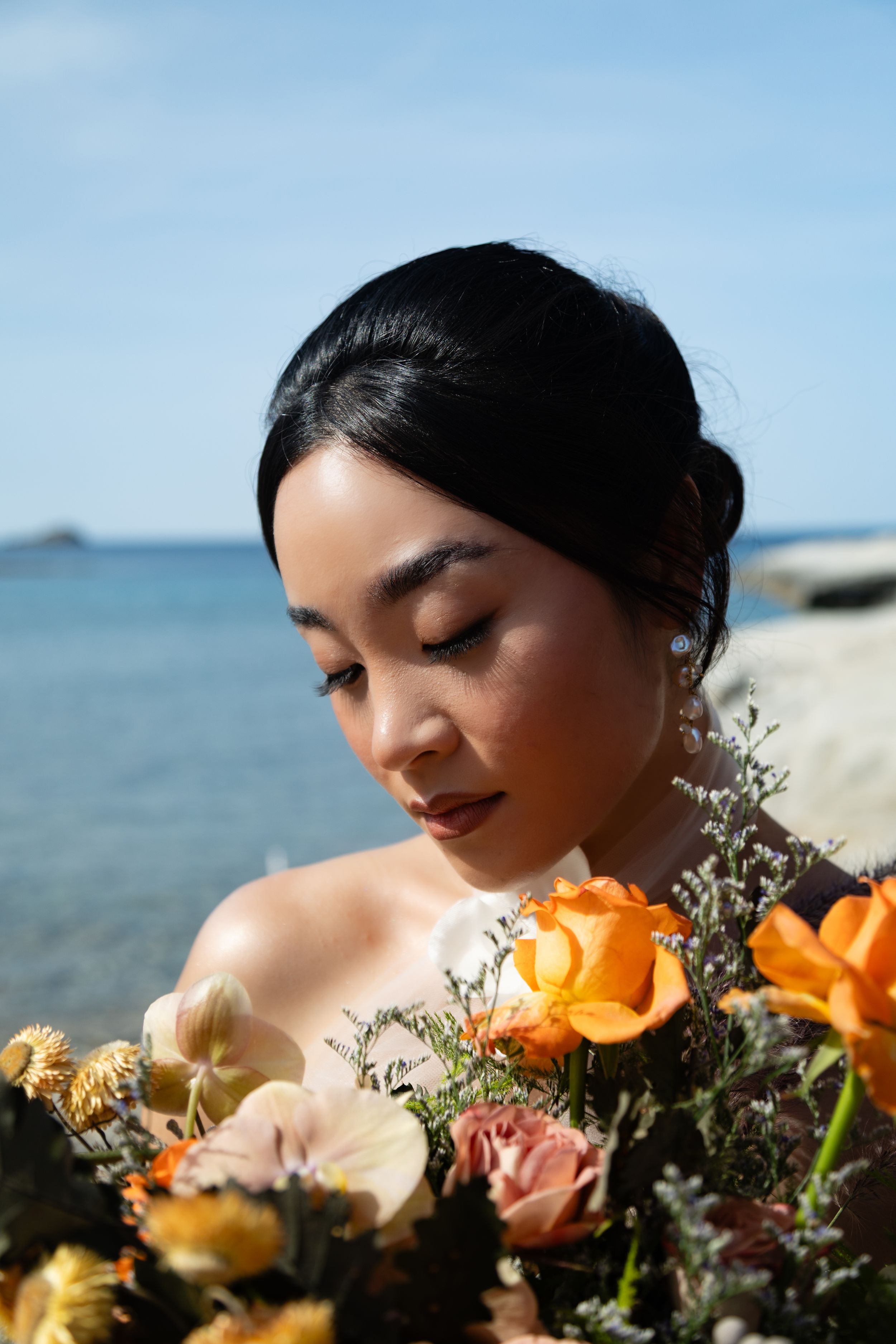 Close-up artistic portrait with orange roses and baby's breath flowers against a coastal backdrop.