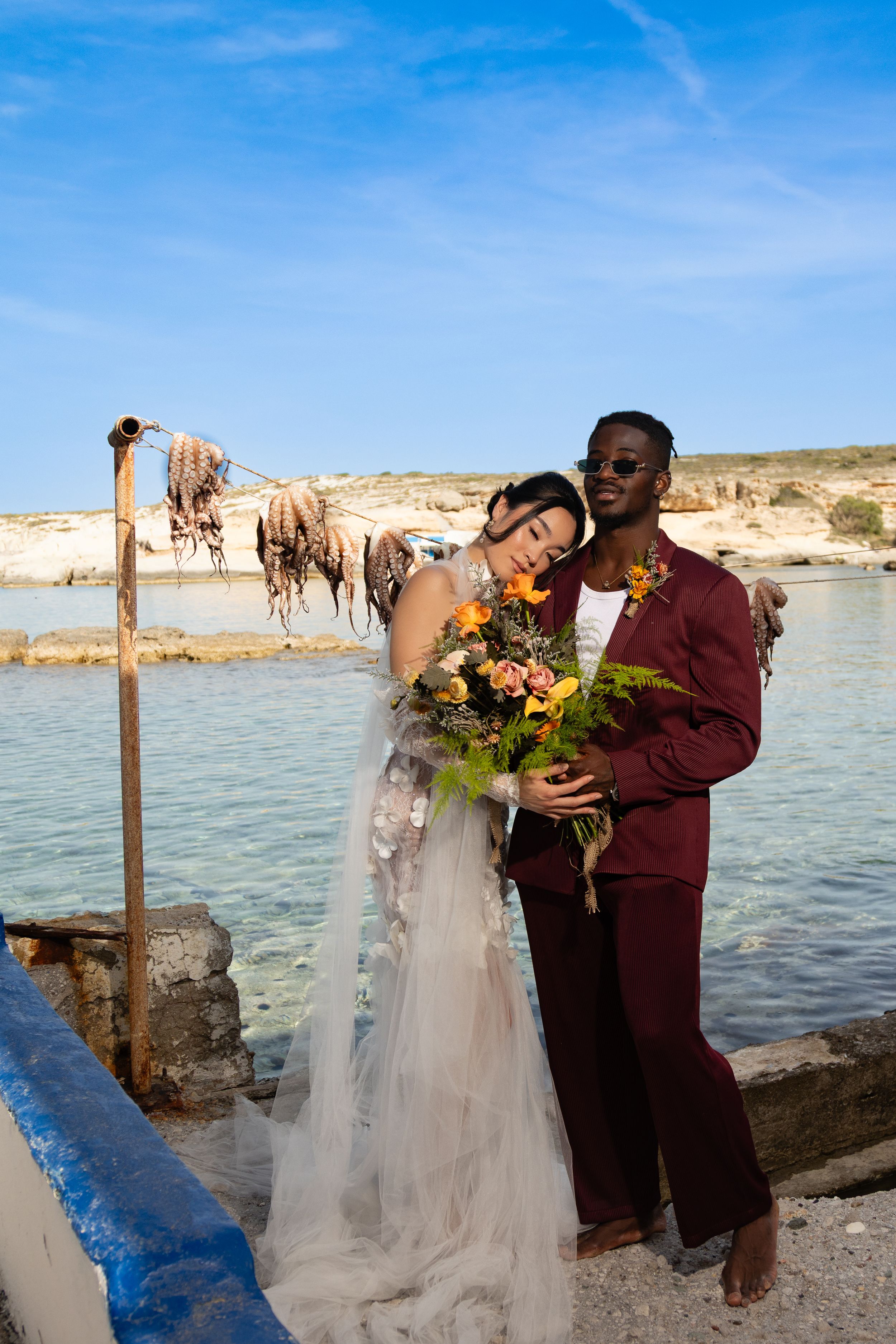 A couple shares romantic moments in wedding attire by a scenic lakeside with rocky cliffs in the background.