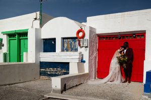 A couple poses in front of colorful doors in a Mediterranean style building with white walls and vibrant green and red doors.