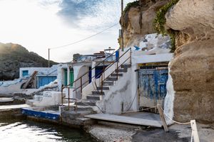 Traditional white fishermen's boat houses with blue doors carved into rocky cliffs along Mediterranean coastal waters.
