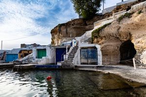 Panoramic series of coastal cave dwellings and boat houses carved into white limestone cliffs along a Mediterranean shoreline.
