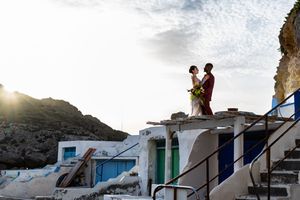 A couple stands on a white rooftop against a dramatic sunset sky in Santorini, Greece.
