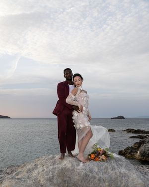 A couple poses for romantic wedding photos on rocky coastal cliffs at sunset with ocean views in the background.