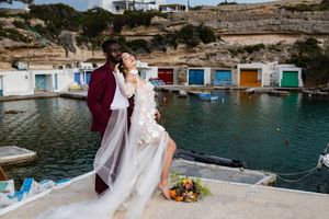 A couple poses together by colorful boat houses along a Mediterranean coastal inlet during a wedding photoshoot.