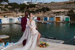 Scenic Mediterranean boat houses with colorful doors line the rocky coastline of a tranquil blue water harbor.