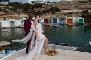 A romantic scene unfolds by vibrant boat houses and turquoise waters at a Mediterranean coastal location.