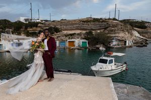Scenic coastal wedding photoshoot with boats and rocky cliffs in the background by turquoise Mediterranean waters.