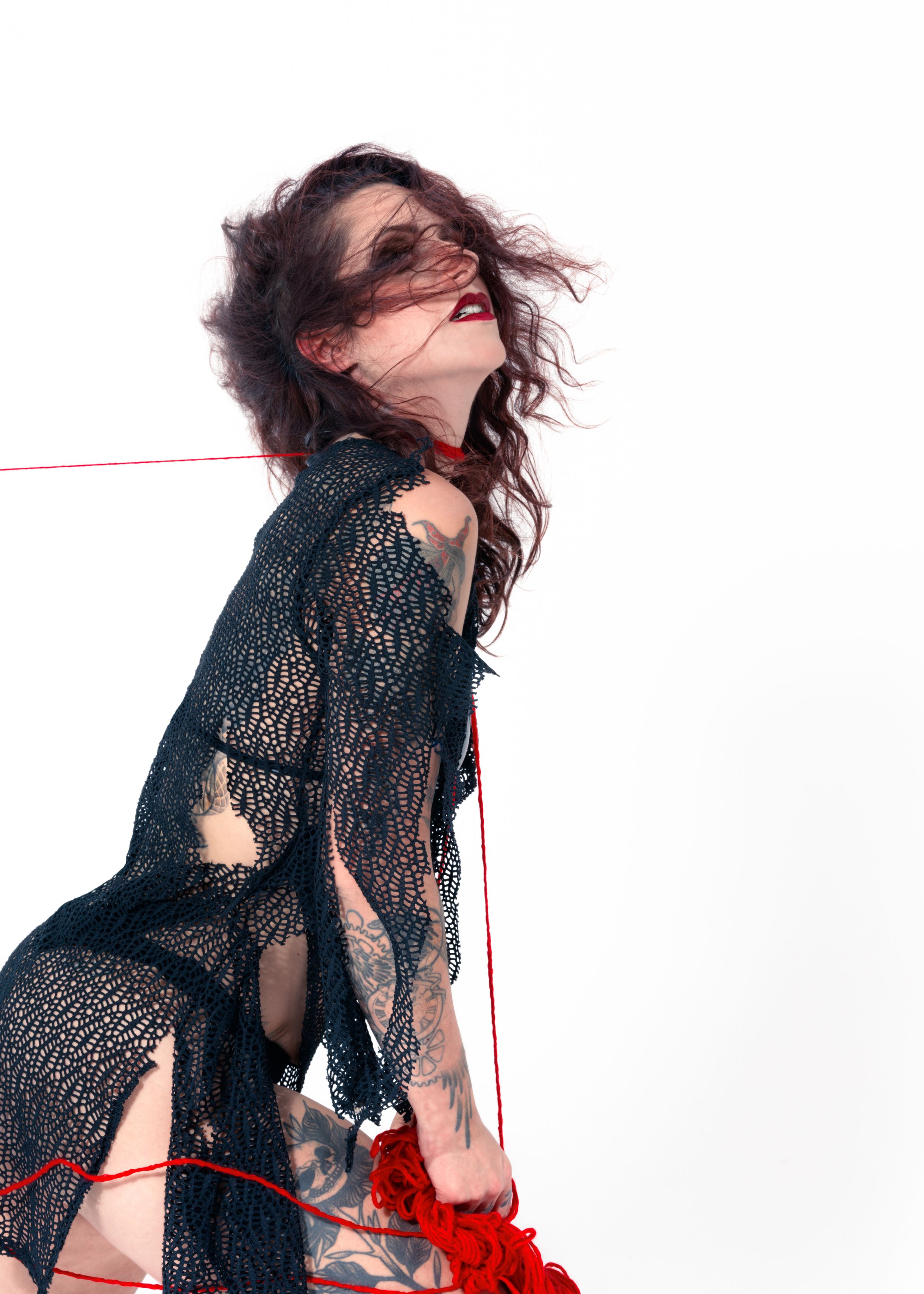 Editorial portrait of a model in black lace lingerie in a dynamic pose with a red cord prop on a white backdrop