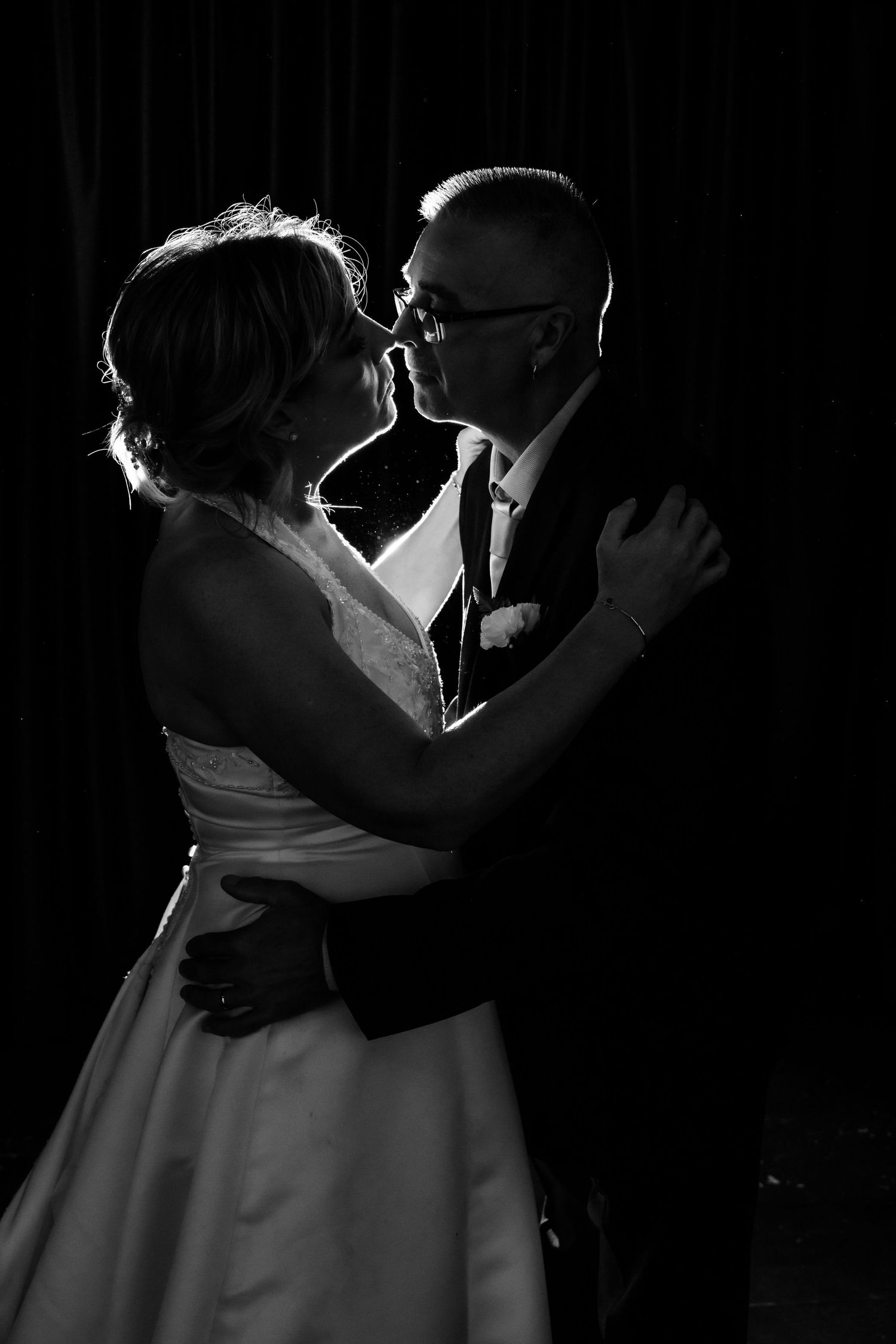 A romantic black and white wedding photo captures an intimate dance with dramatic backlighting.