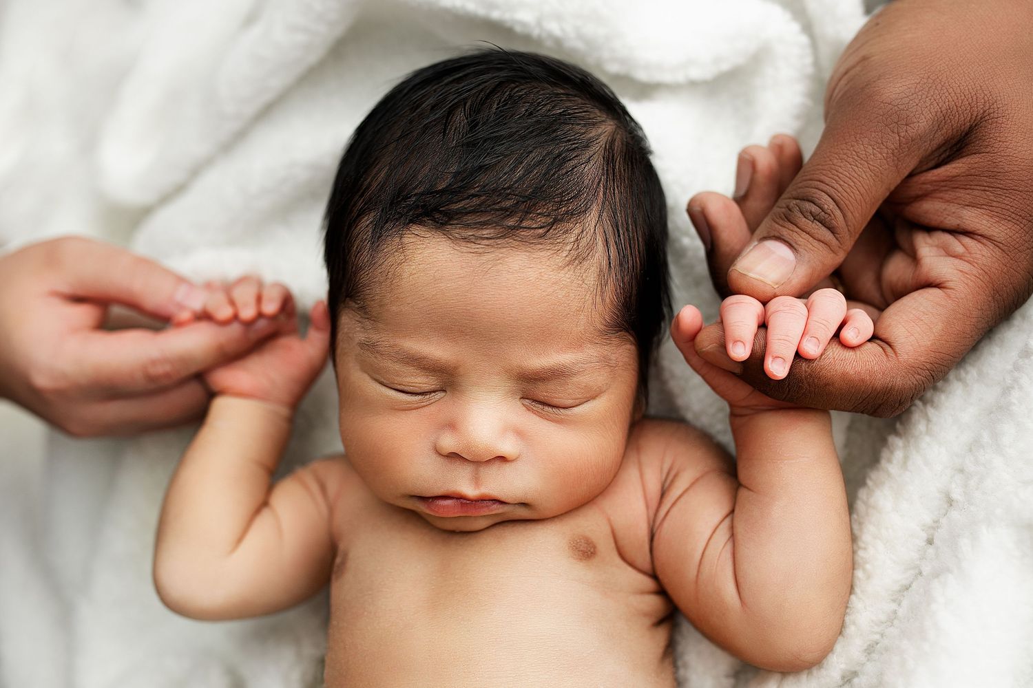 Sweet sleeping baby swaddled in white blanket rests peacefully on soft textured surface. In-home newborn photography sessions.