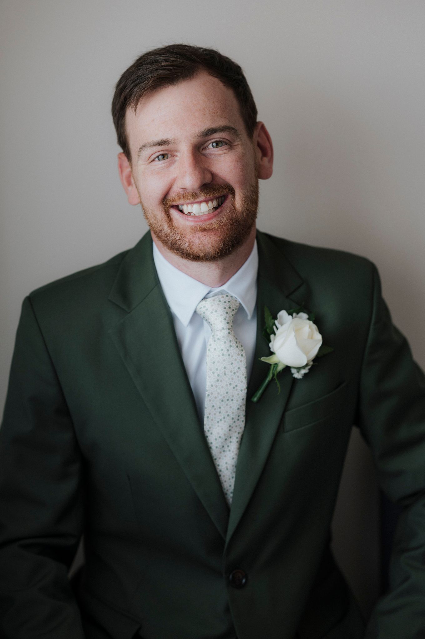A series of close-up portraits showing a person in a dark green suit with a white tie and boutonniere against a gray background.