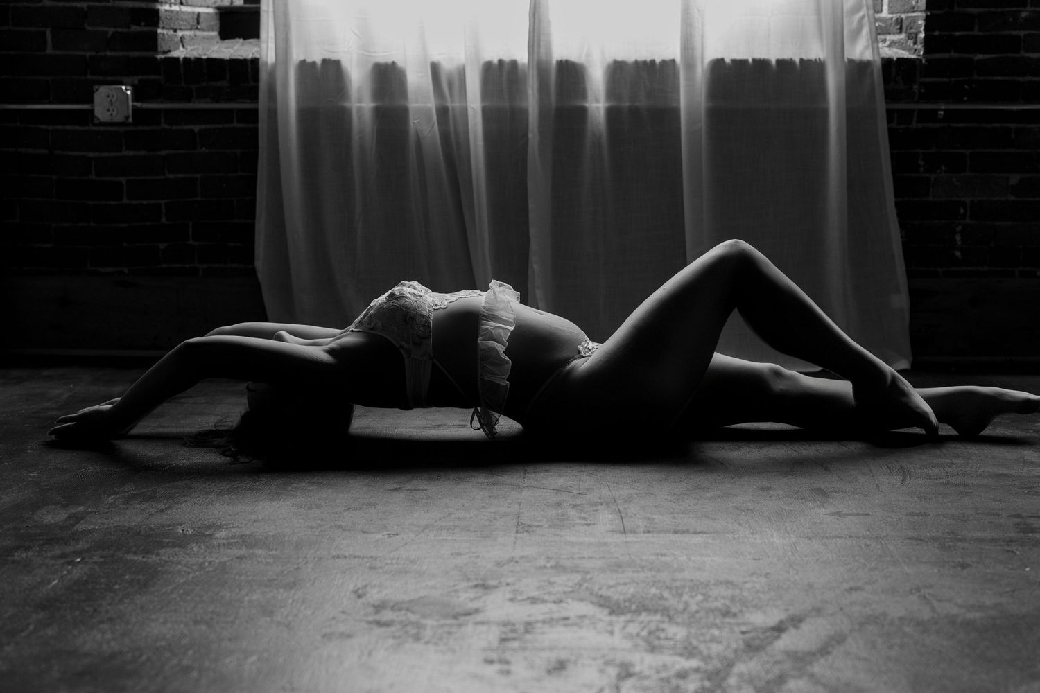 A black and white cinematic shot shows a dark silhouette lying on the floor against a bright window in a dramatic mood.