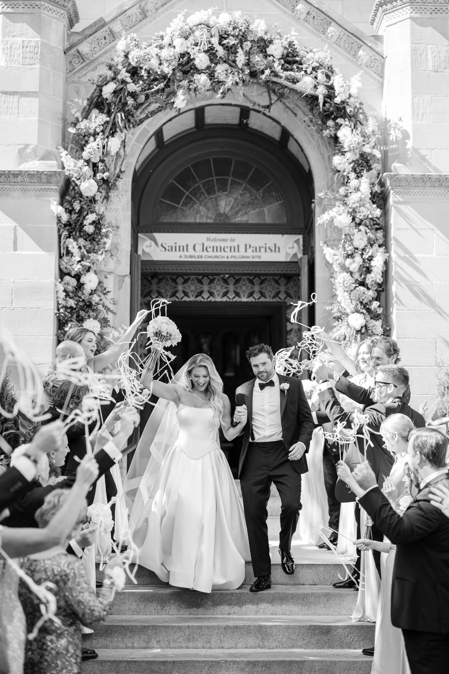 Newlyweds share intimate moment in sunlit outdoor setting with bride wearing flowing veil and white beaded gown.