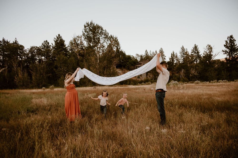 Professional outdoor photoshoot in tall grass with a flowing white veil creating ethereal movement in nature.