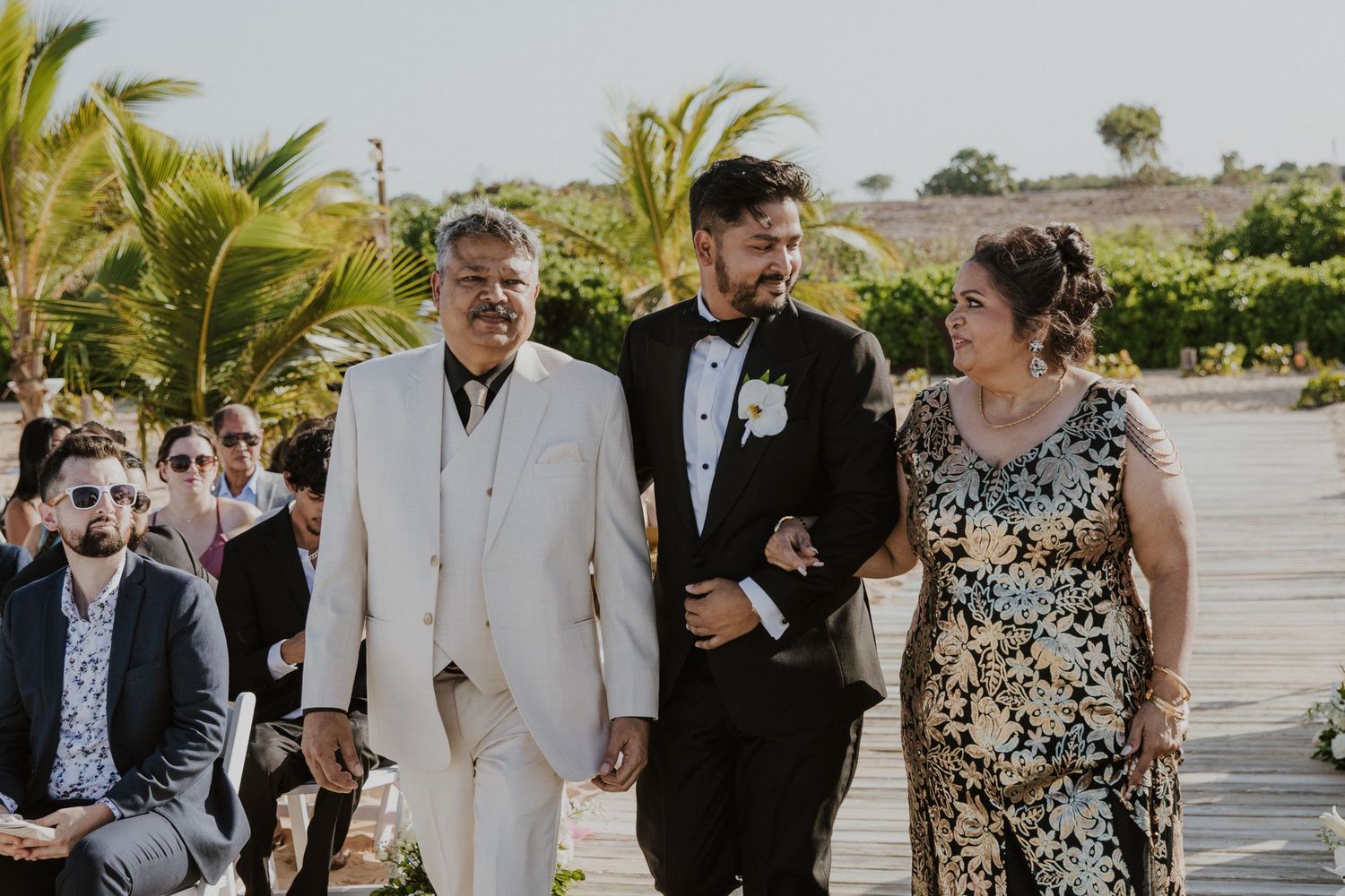 Wedding party guests mingling outdoors under palm trees at tropical destination venue.