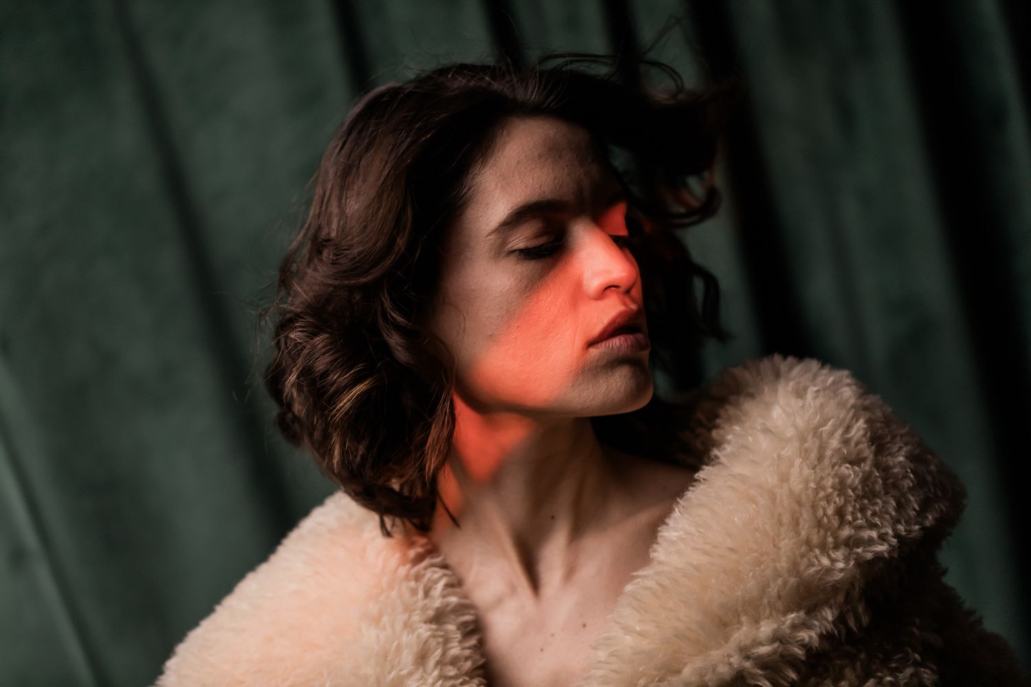 Dramatic red lighting illuminates a person in a cozy cream sherpa jacket against a dark green backdrop.