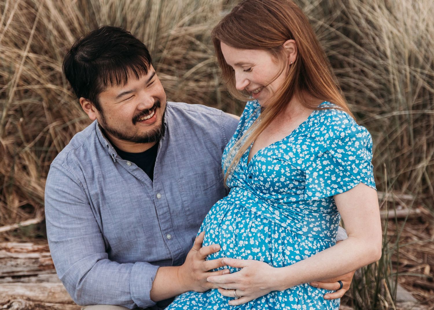 Close-up of couple's hands resting on pregnant belly in black dress against outdoor backdrop during sunset.