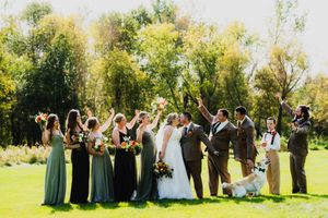 A wedding party stands in a row on a sunlit green lawn with trees in the background during an outdoor ceremony.