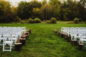 White wedding chairs arranged in rows on a lush green lawn with forest trees in the background for an outdoor ceremony.