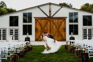 White modern barn wedding venue with large wooden sliding doors and rows of white chairs set up on green lawn for ceremony.