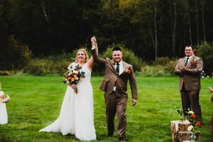 A joyful wedding celebration with the newlyweds raising their arms in celebration on a lush green lawn surrounded by trees.