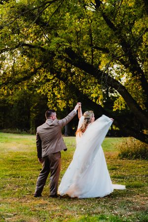 A couple dances together in an outdoor autumn setting beneath trees with golden foliage.