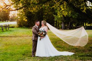 A flowing white veil catches the autumn breeze in an outdoor wedding scene at sunset.