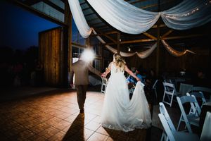 Wedding couple dances together beneath soft draped fabric in a rustic barn venue with romantic lighting.