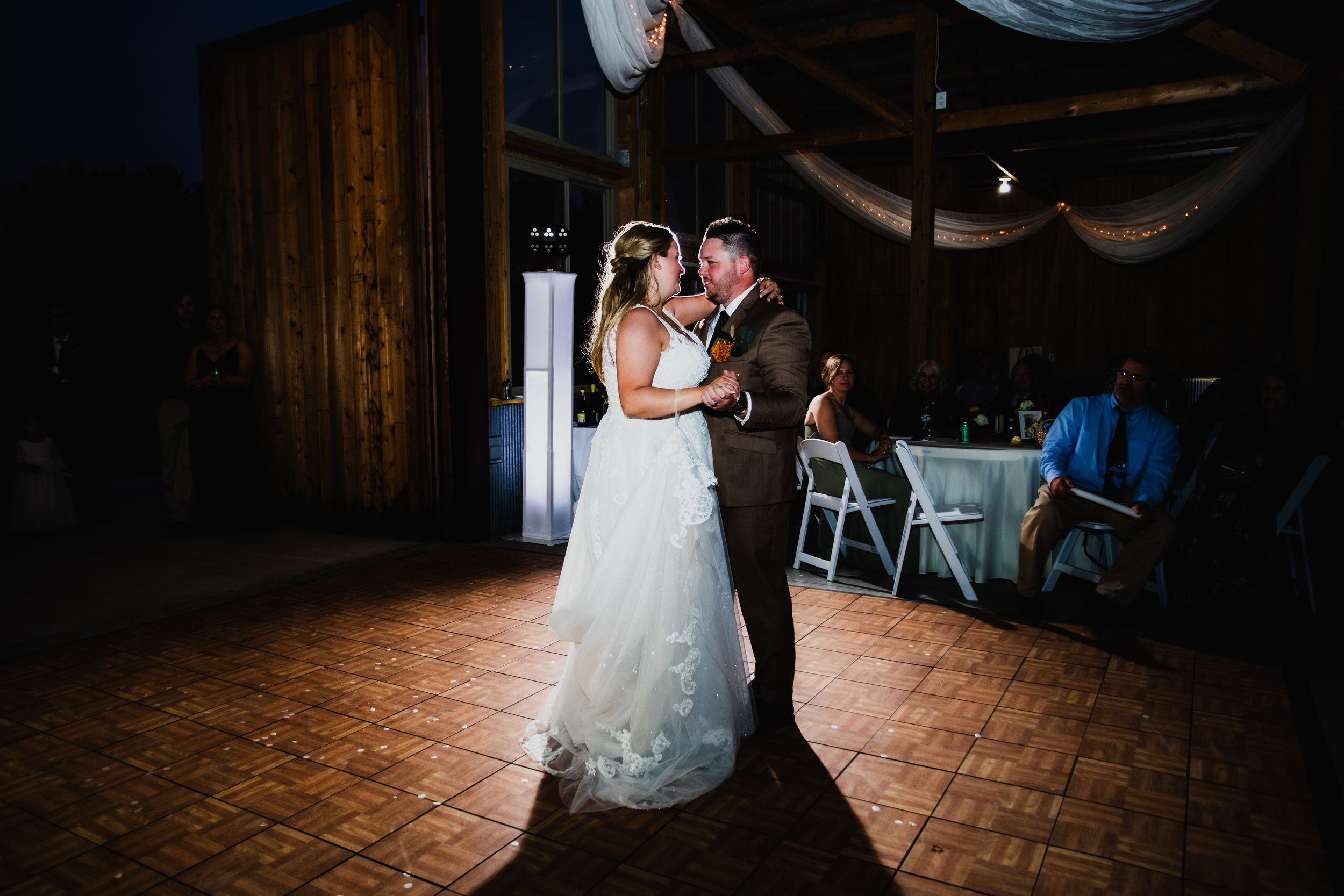 A couple shares their first dance together in an elegantly decorated rustic barn venue with wooden floors and draped fabric.