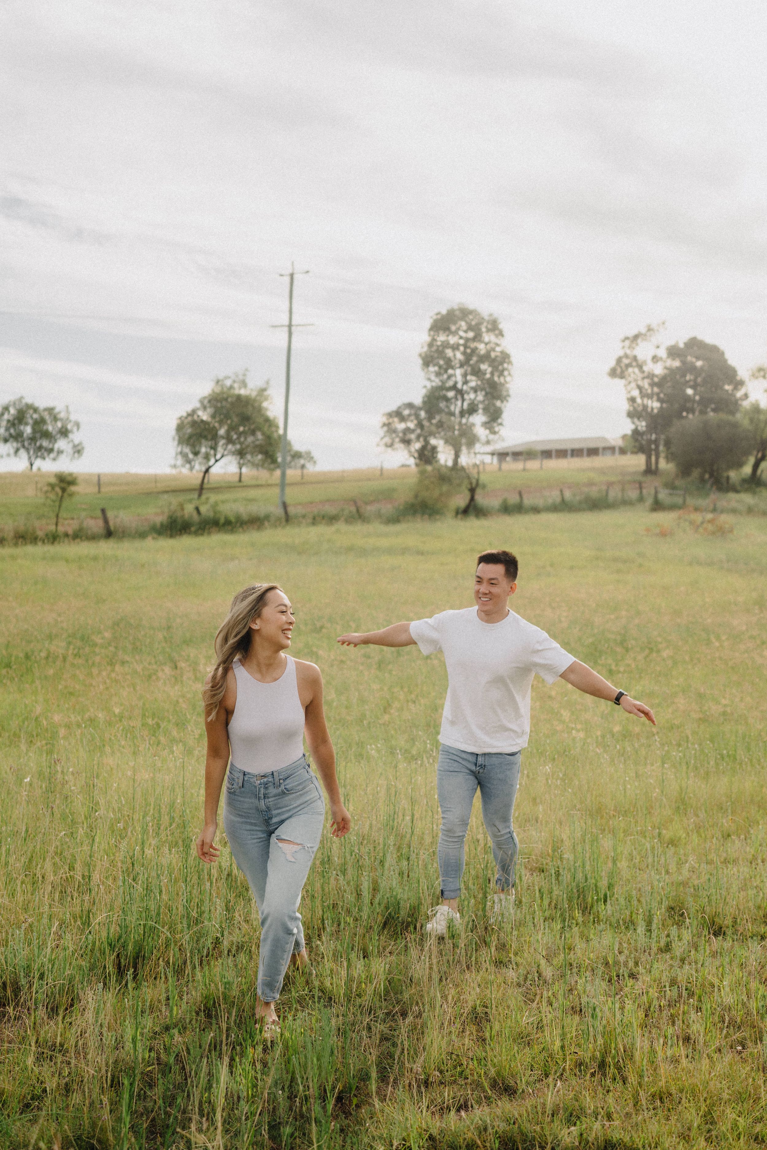 A playful couple spends time together in a sunny grassy meadow on a cloudy afternoon.