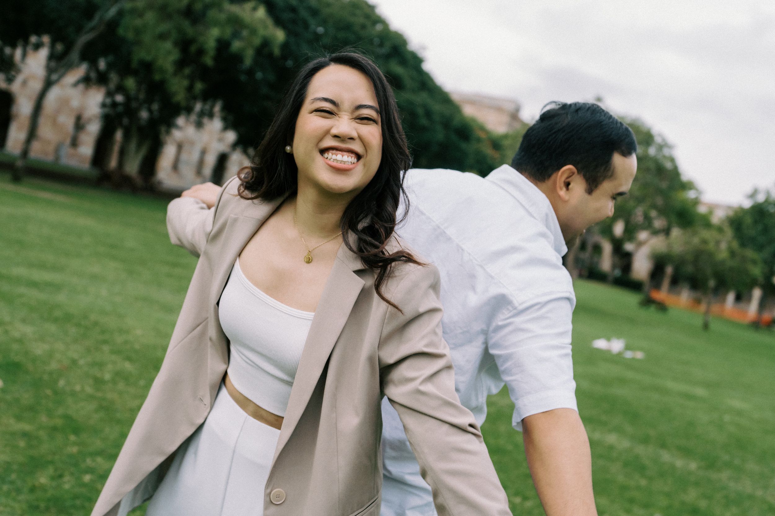 A romantic moment shared between a couple in formal attire on a green lawn during a sunny outdoor photoshoot.