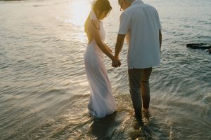 A couple embraces intimately on the beach during golden hour as sunlit waves gently roll onto the shore.