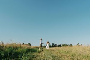 Two people stand together on a grassy hilltop against a bright blue sky on a sunny summer day.